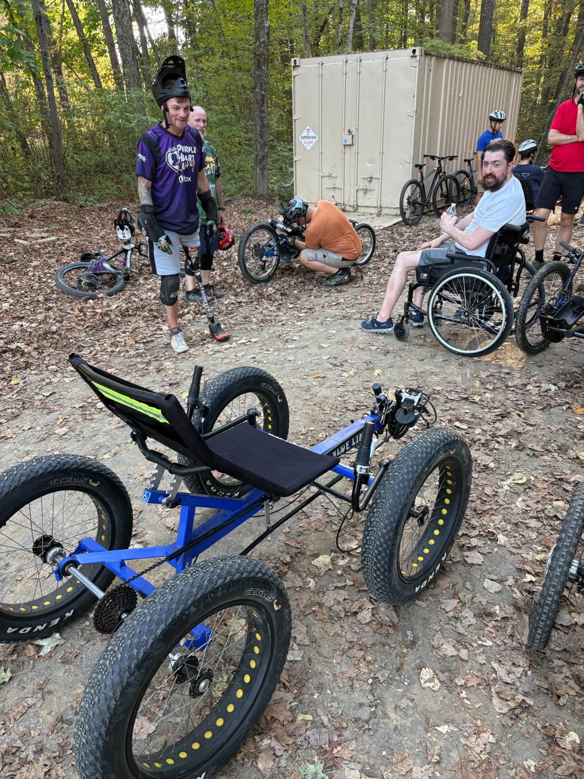 Cyclists and adaptive riders gathered with mountain bikes and adaptive cycles on a wooded trail