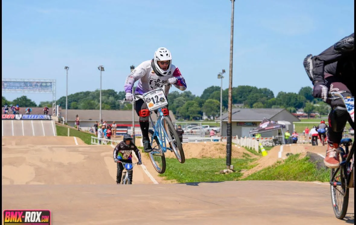 A BMX rider airborne above an outdoor racecourse with other racers behind