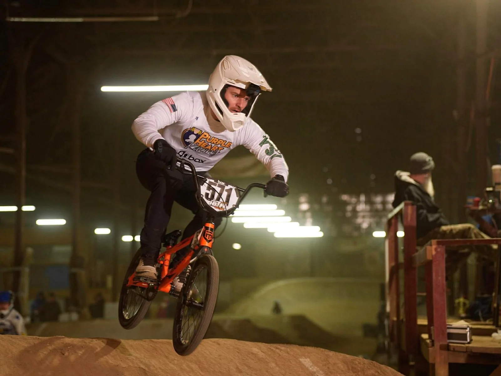 A BMX rider in a white jersey jumping on an indoor track