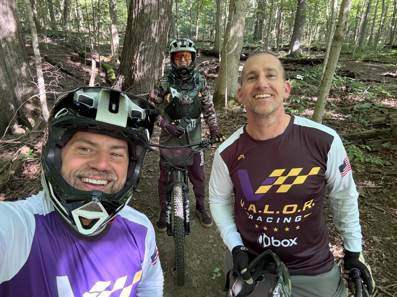 Three smiling riders together with mountain bikes on a wooded trail