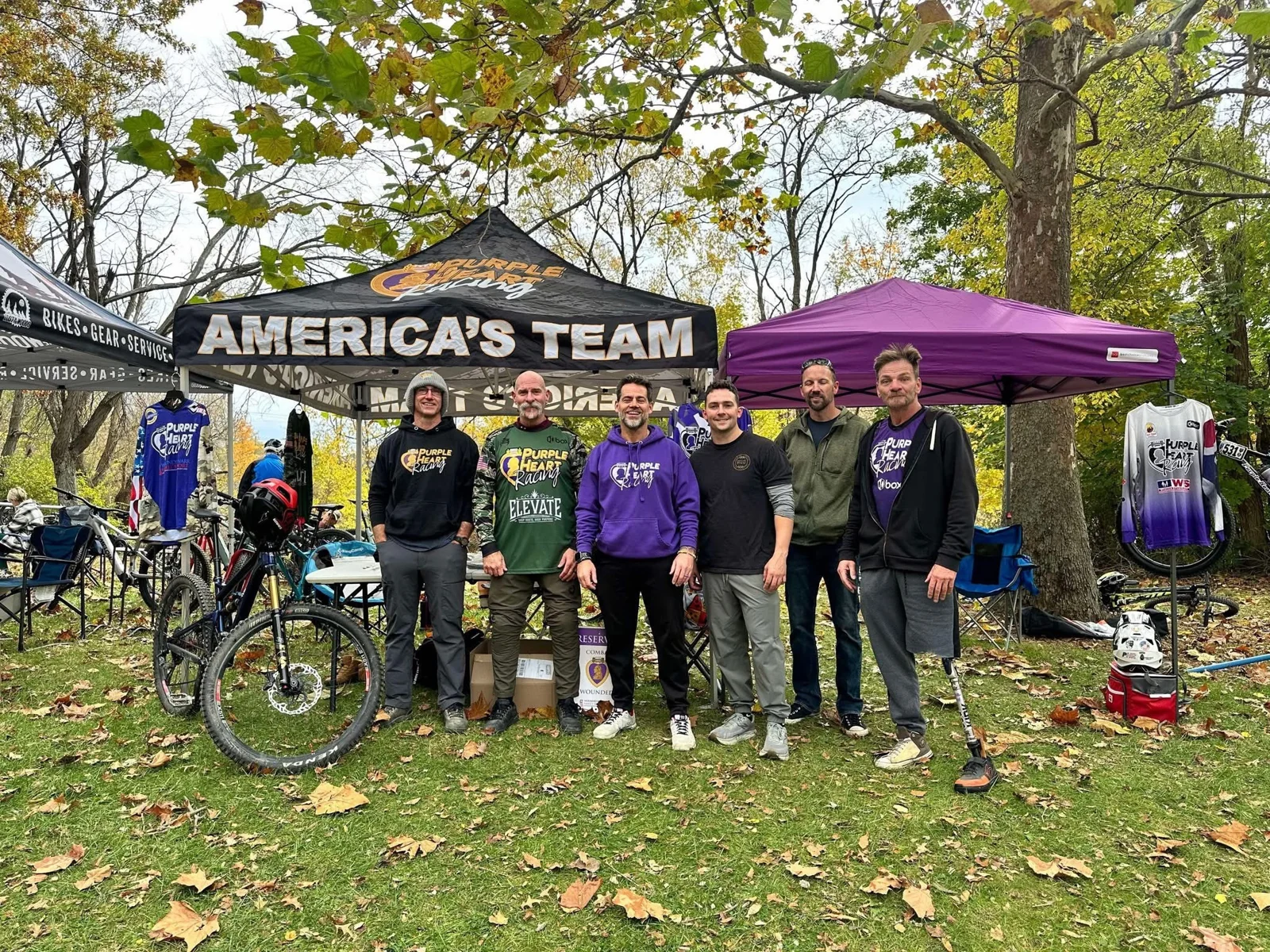 Team members gathered beneath team tents with bikes at an outdoor event